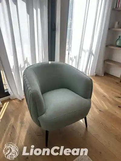 Sivozelena tapacirana fotelja sa zaobljenim naslonom pored prozora