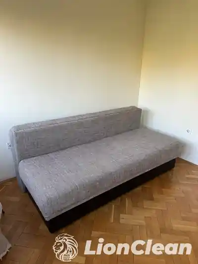 Sivi lezaj sa niskim naslonom i tamnim donjim delom uz zid